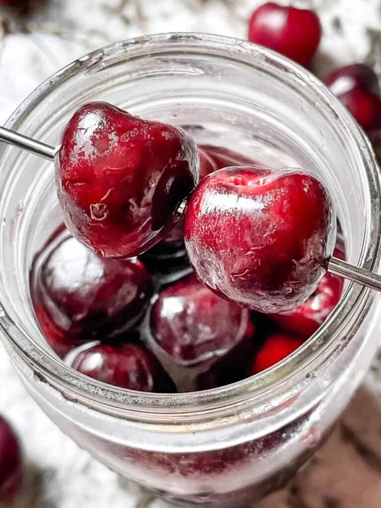 A skewer of Brandied Cherries on top of the jar