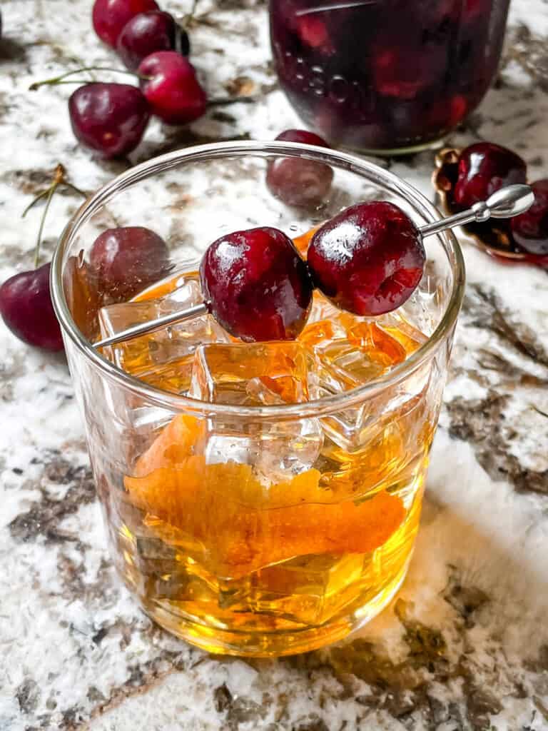 A skewer of Brandied Cherries on top of a cocktail