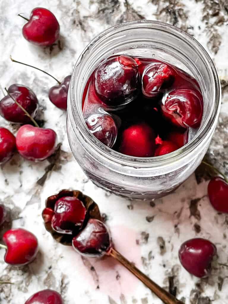 A jar of Brandied Cherries with cherries around it