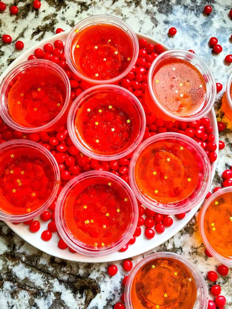 A round plate filled with little cinnamon candies and the shot cups on top, from top view