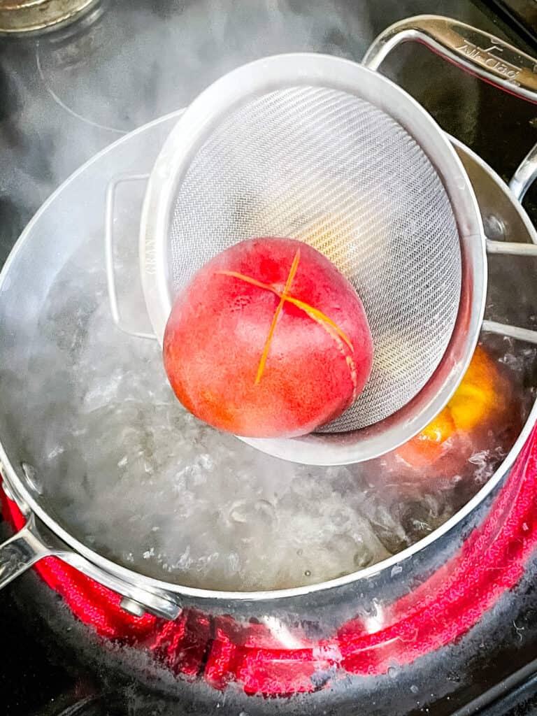 A strainer scooping a peach from boiling water
