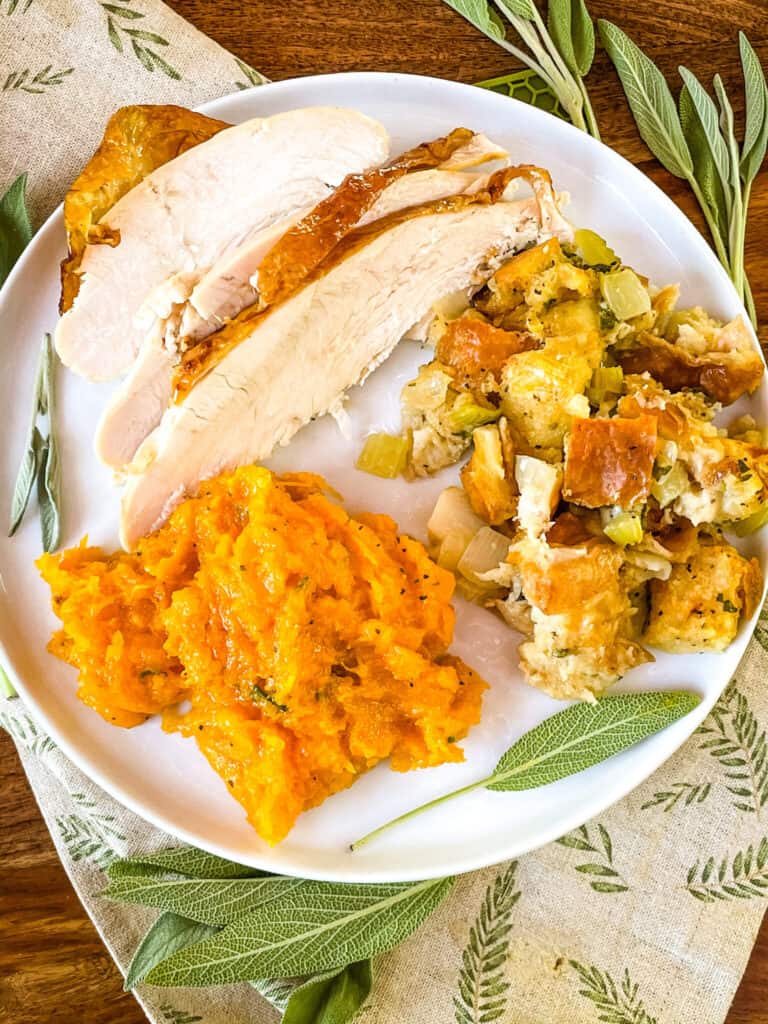 A white plate from the top with sage stuffing, turkey, and mashed squash.