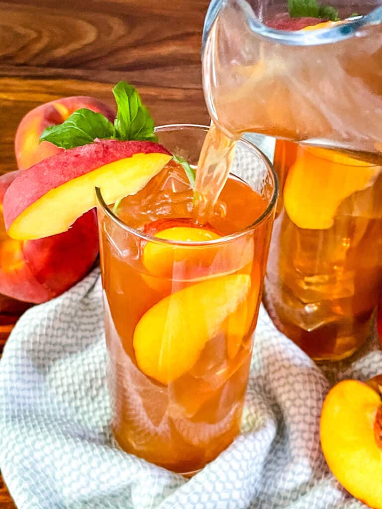A pitcher pouring a tall glass of Peach Tea