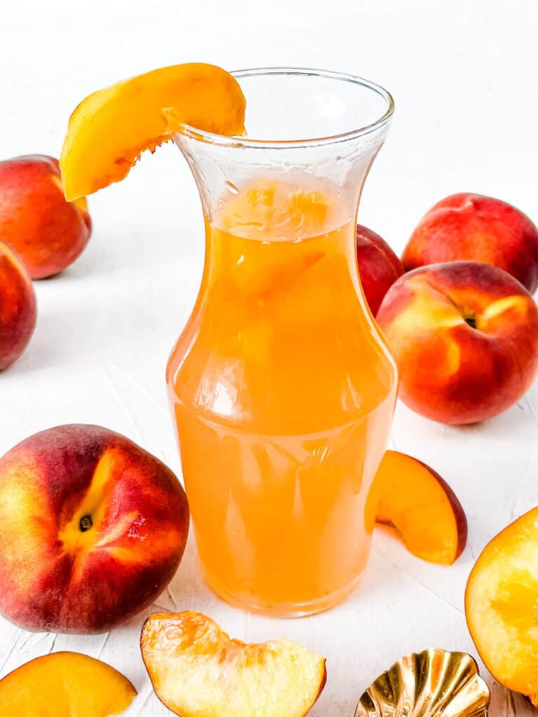 A jar full of Peach Syrup with peaches around it