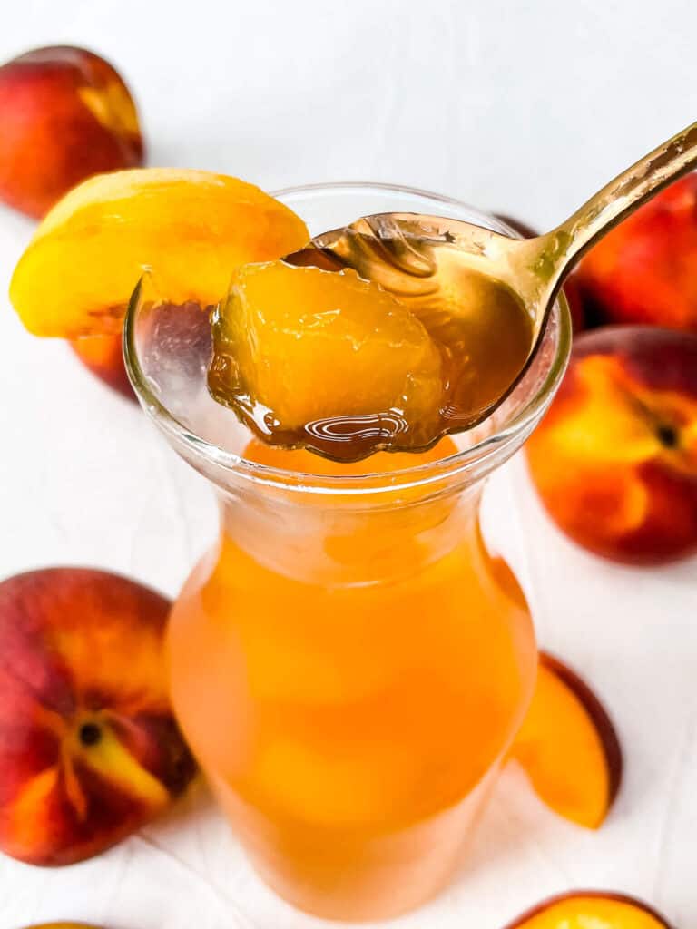 A spoon scooping the syrup and a piece of peach out of the jar