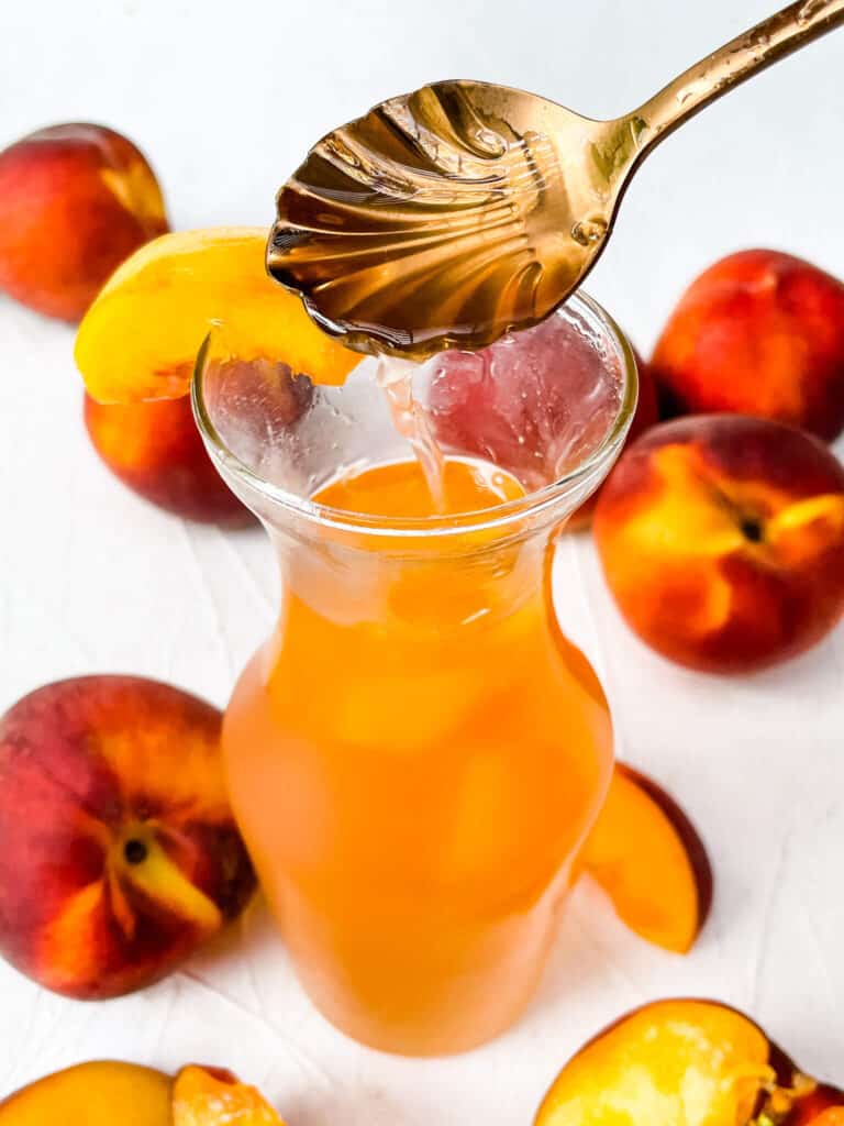 A spoon dripping Peach Syrup into the jar