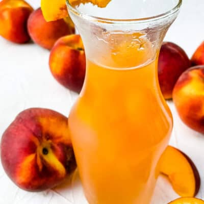 A jar of Peach Syrup with peaches around it