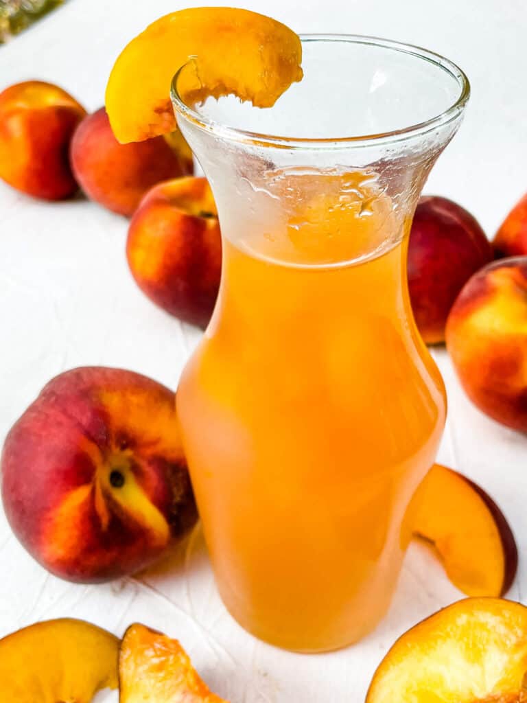 A jar of Peach Syrup with peaches around it