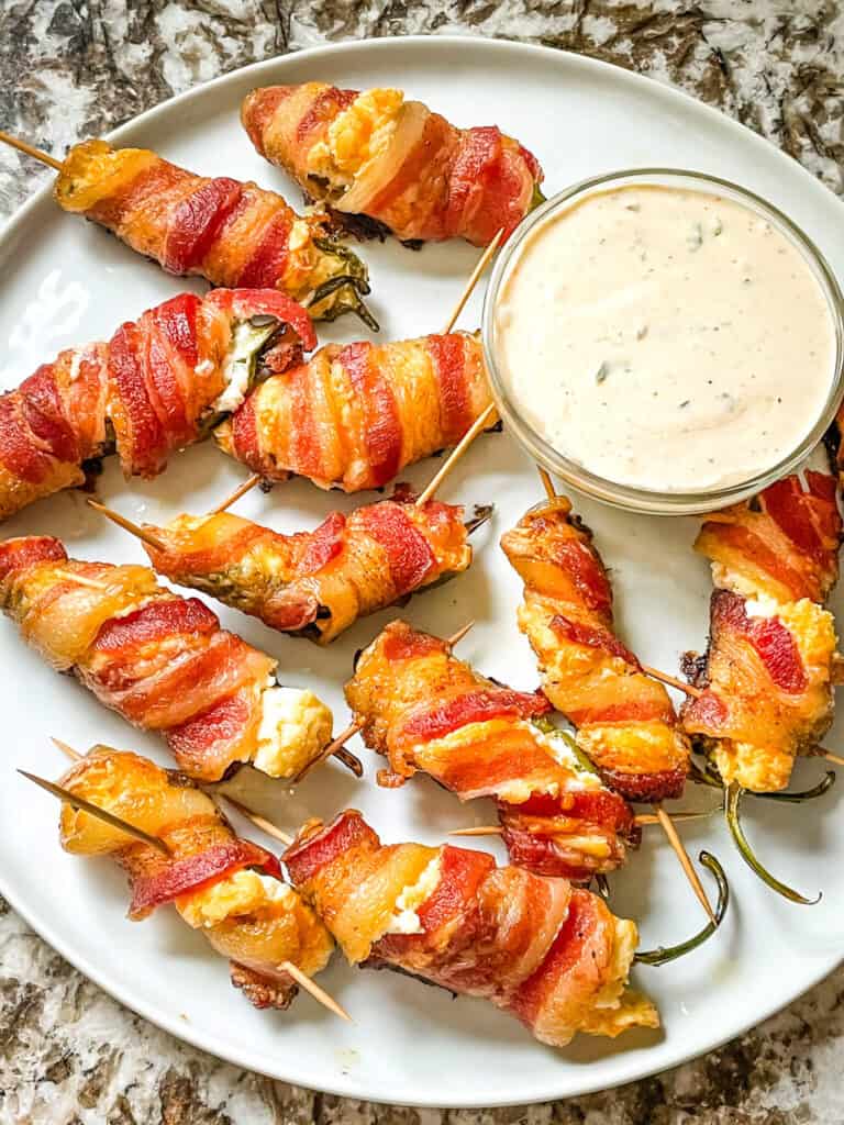 A white plate filled with Smoked Jalapeno Poppers and dipping sauce