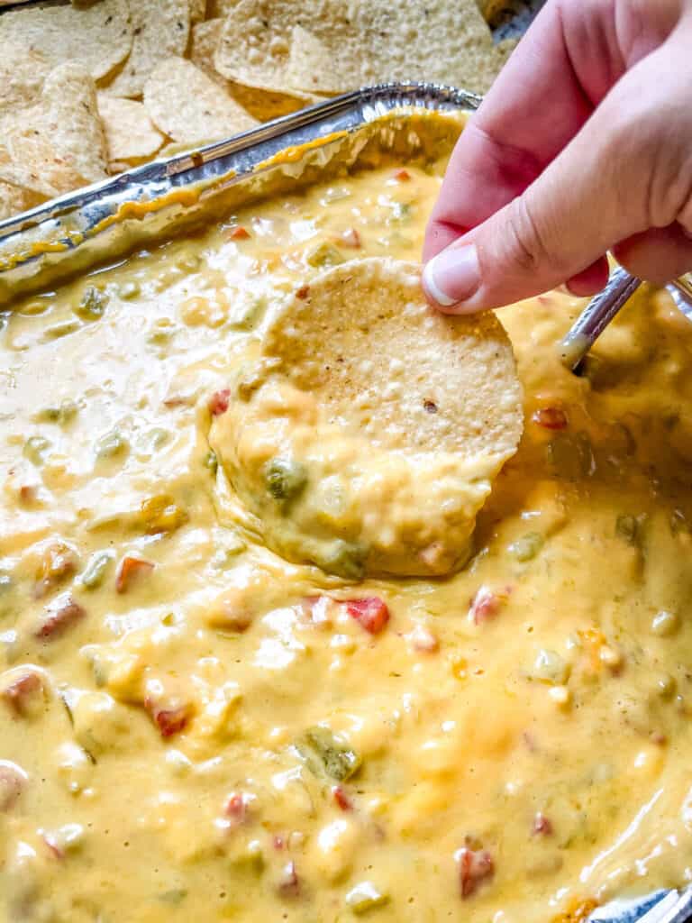 A hand digging a chip into a pan of Smoked Queso