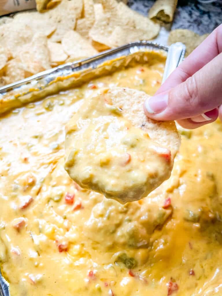 A hand holding a chip that has been dunked in the queso