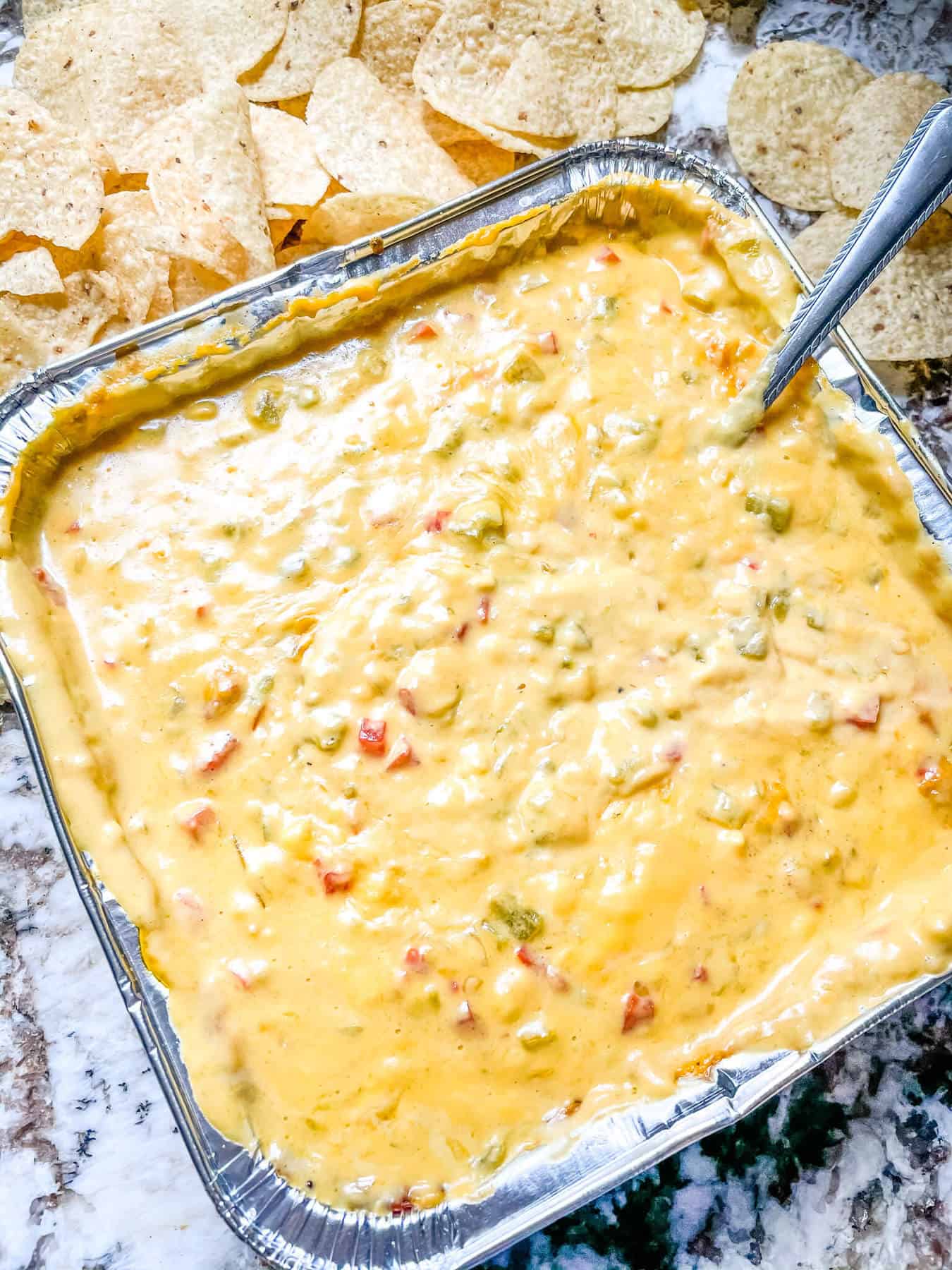 A foil pan full of melted Smoked Queso with chips
