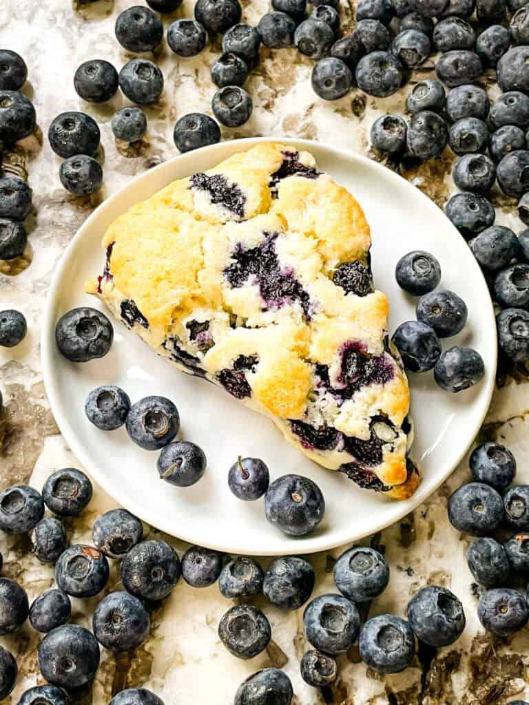 A scone on a plate surrounded by a lot of berries