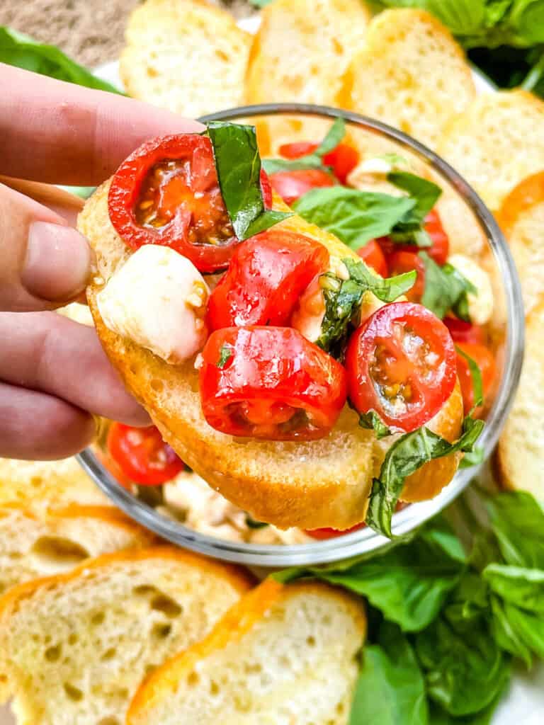 A hand holding a piece of Bruschetta with Mozzarella (Caprese Bruschetta)