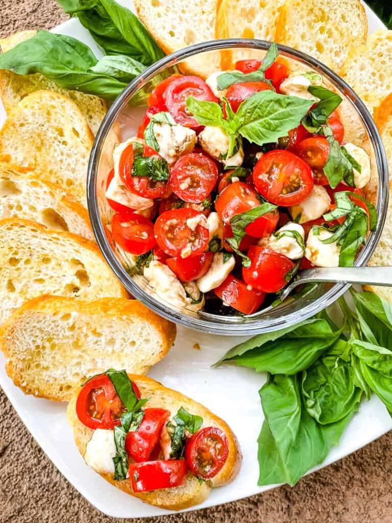 The tomato mixture in a bowl with crostini and one piece topped on a white plate