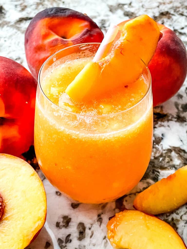 A glass full of the peach drink surrounded by fruit