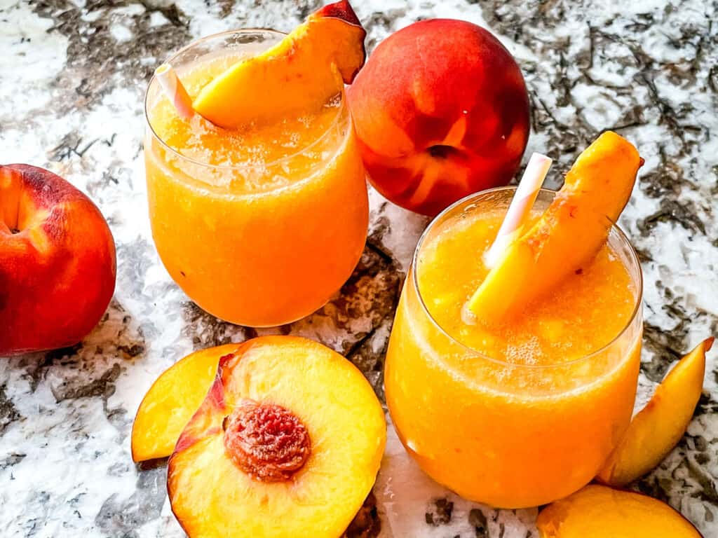 Two Copycat Outback Steakhouse Wallaby Darned Peach Cocktails with peaches on a counter