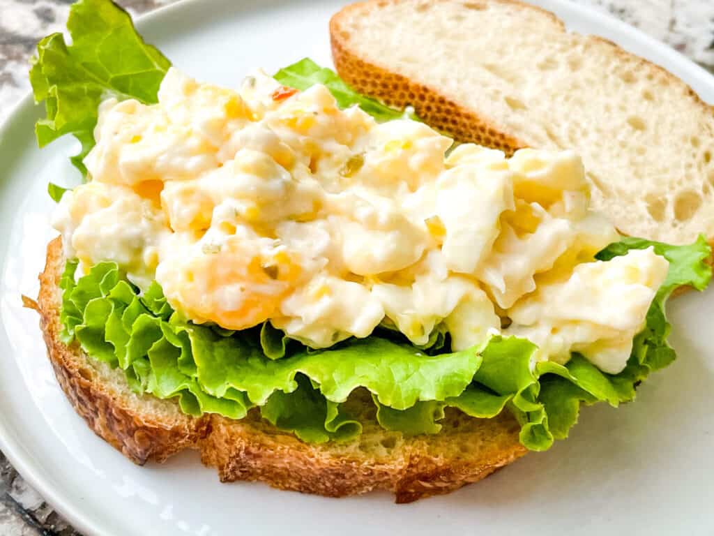 An Egg Salad Sandwich without the top bread piece on a white plate