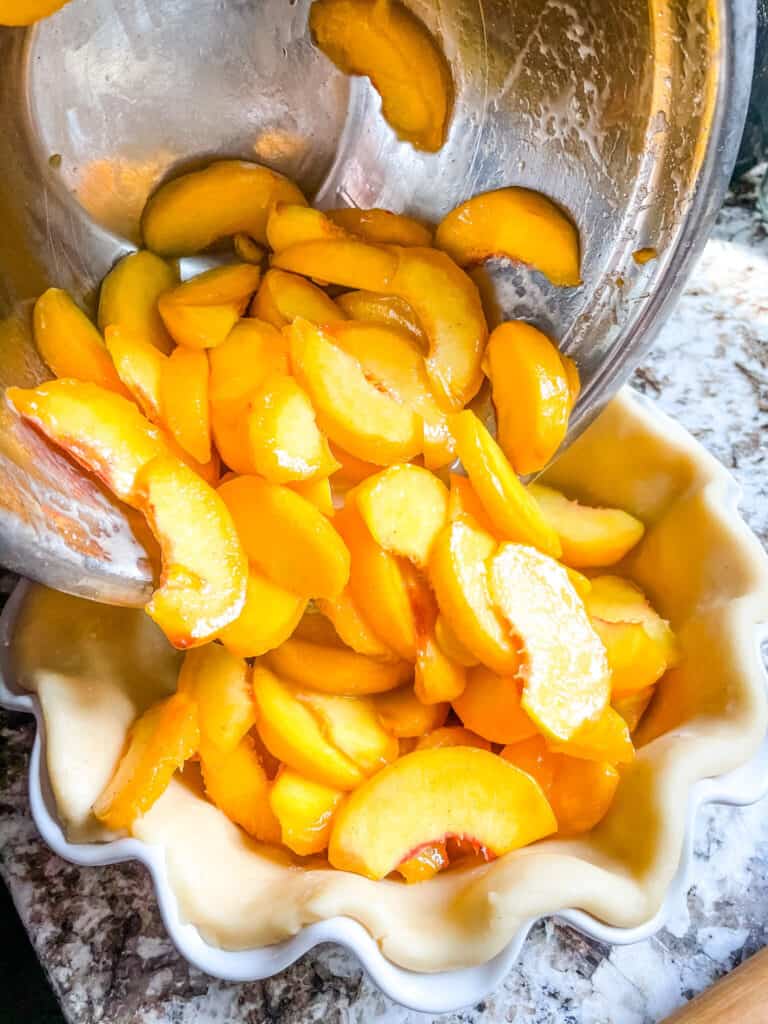 Bowl pouring peach pie filling into the pie dish