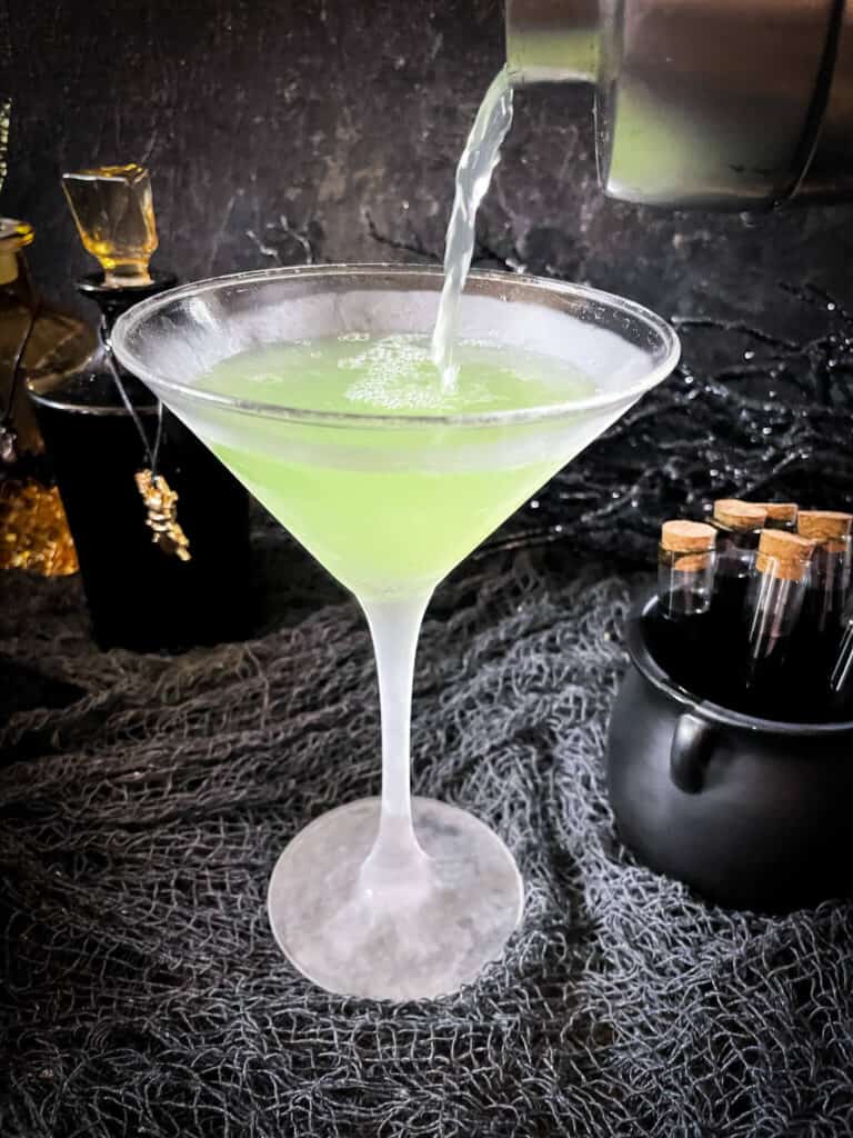 Pouring the green apple mixture into a martini glass