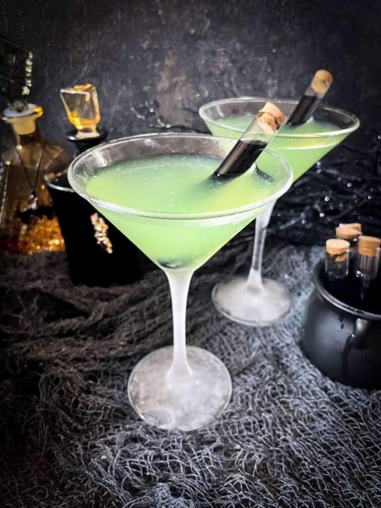 Two martini glasses with the apple mixture and a black poison vial in them