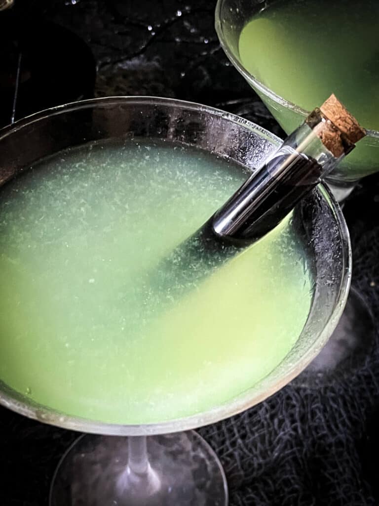 Close up top view of the martini glass with the green liquid and a poison vial in it