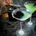 A hand pouring the black poison into a green cocktail