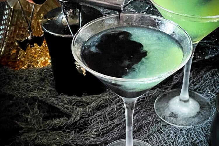 A hand pouring the black poison into a green cocktail