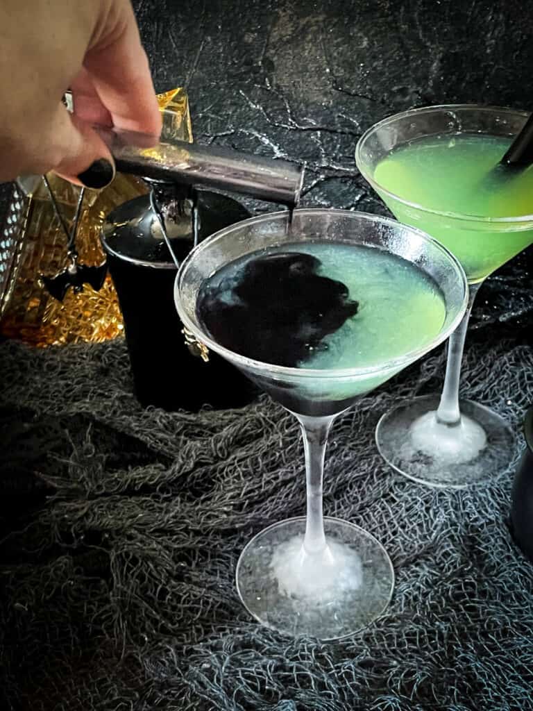 A hand pouring the black poison into a green cocktail
