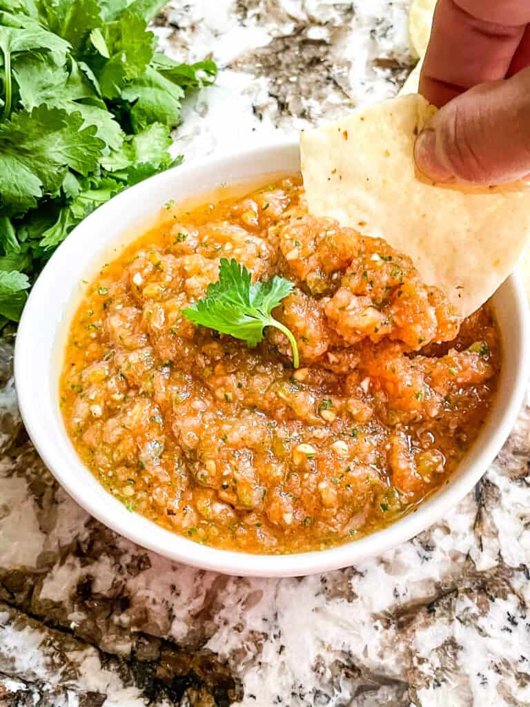 A hand dunking a chip into a bowl of Ranchera Salsa