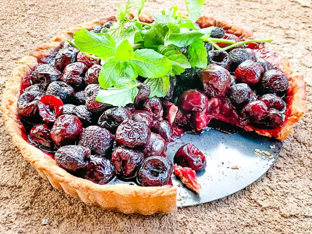 A cherry tart topped with mint and with a piece missing