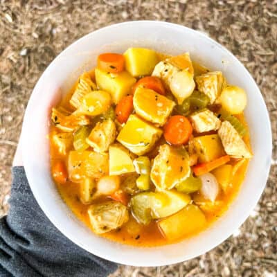 A hand holding a bowl of Chicken Campfire Stew from the top view