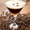 A glass full of the coffee cocktail with beans all around it