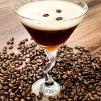 A glass full of the coffee cocktail with beans all around it