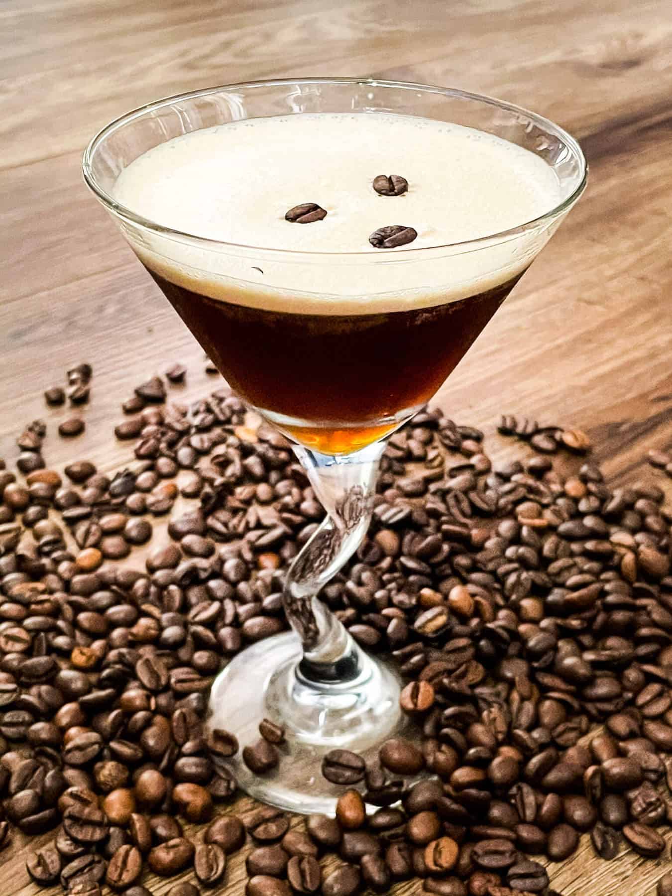 A glass full of the coffee cocktail with beans all around it