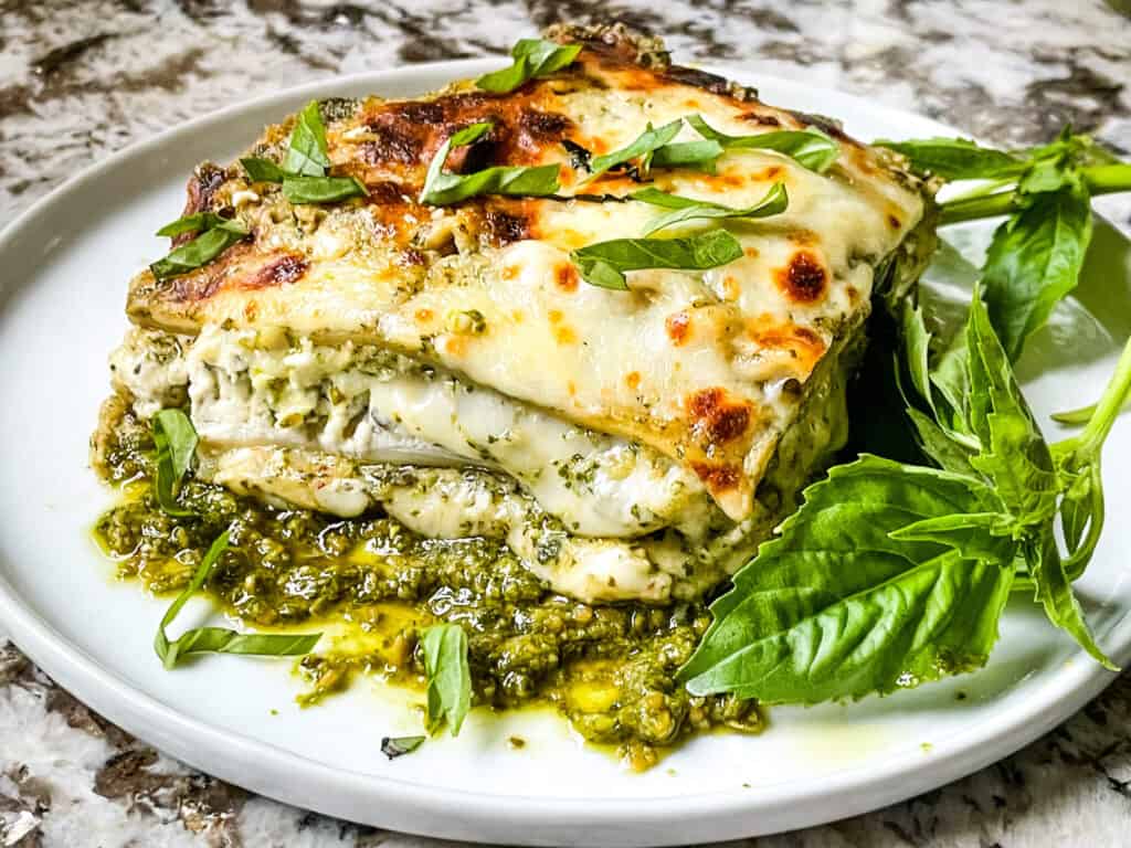 A slice of Lasagna al Pesto on a white plate with fresh basil