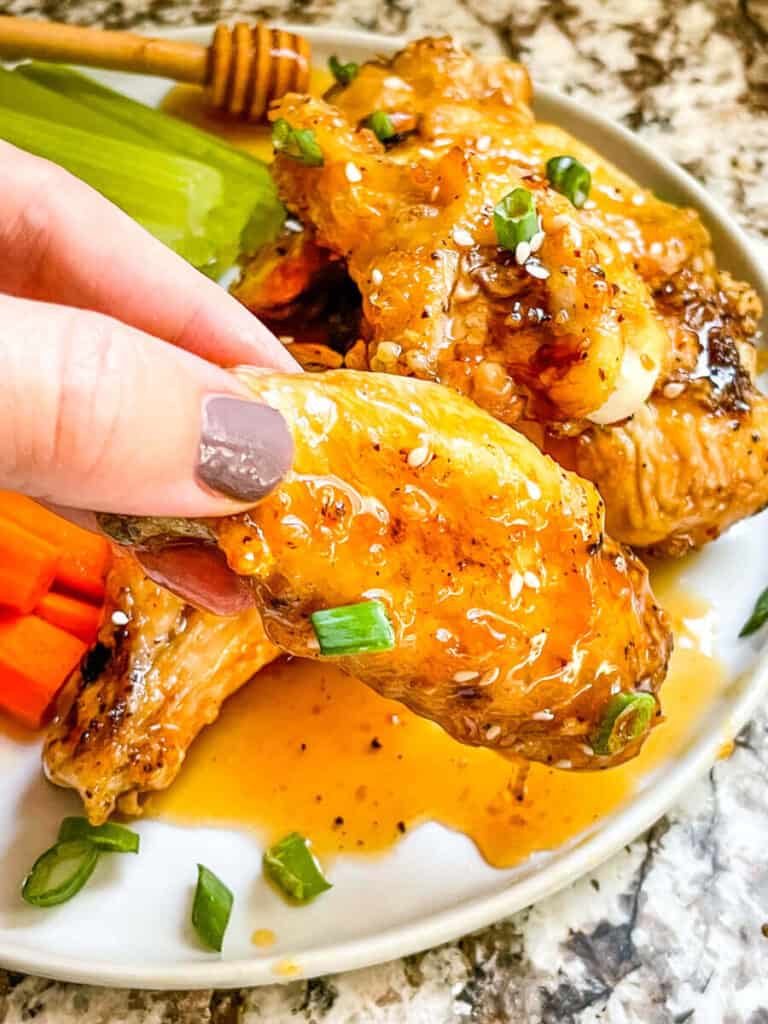 A hand grabbing a wing from the plate