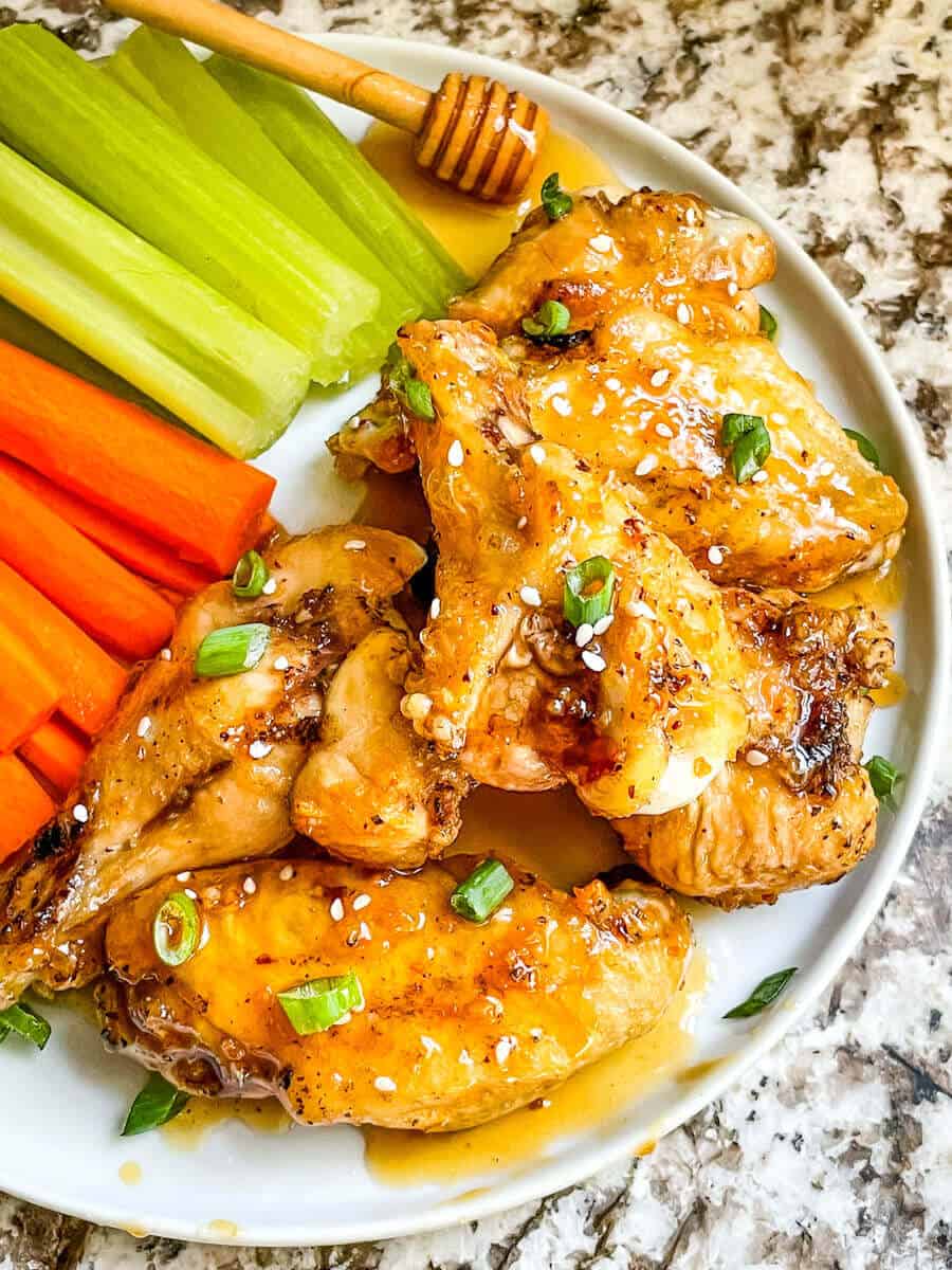 Top view of Honey Garlic Chicken Wings in a pile on a plate with carrots and celery