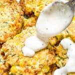 A spoon pouring white gravy over Corn and Zucchini Fritters