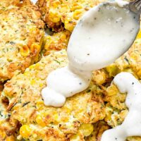 A spoon pouring white gravy over Corn and Zucchini Fritters