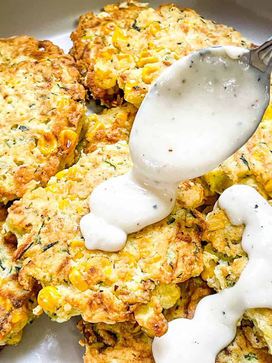 A spoon pouring white gravy over Corn and Zucchini Fritters