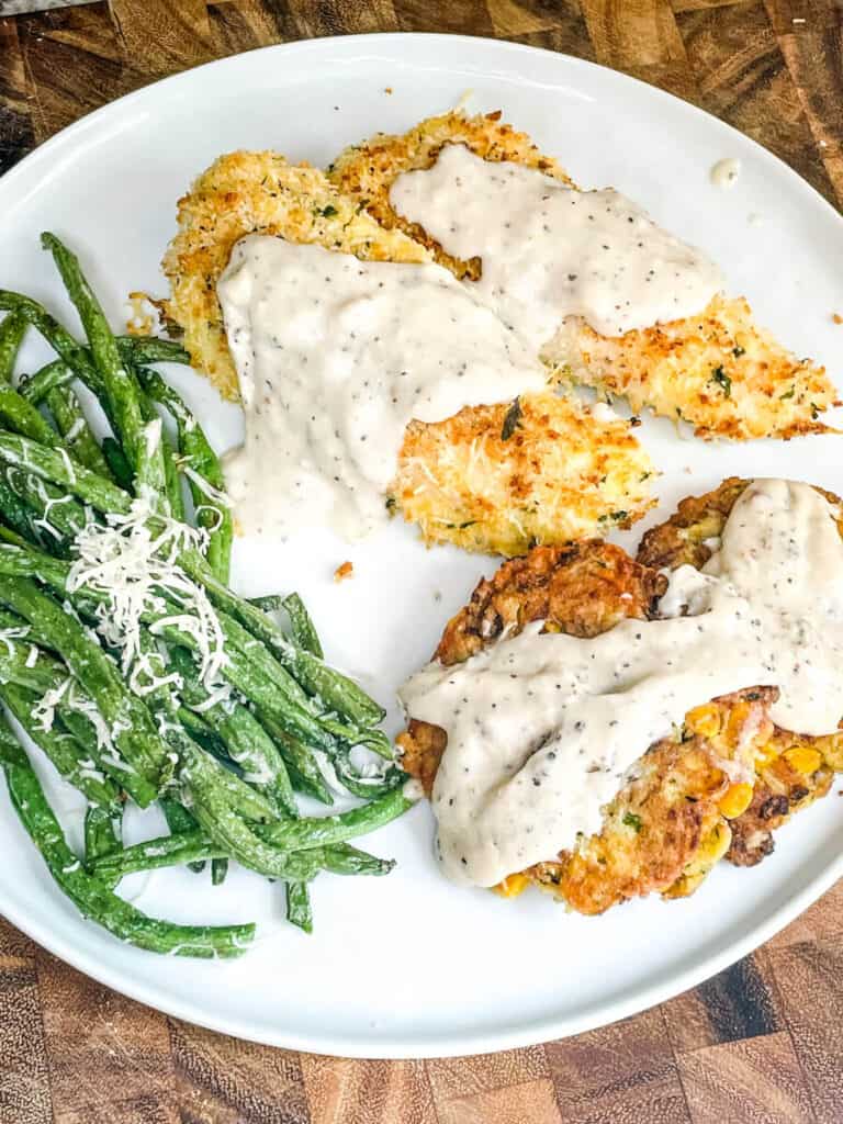 White plate with White Gravy on Parmesan Chicken Tenders and Zucchini Corn Fritters with Green Beans