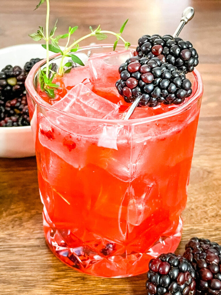 Blackberry Bourbon Sidecar in a clear glass with thyme and berry garnish