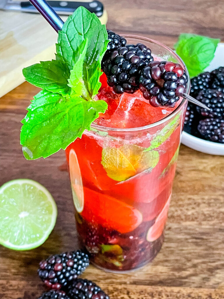 Tall glass of Blackberry Mojito with berries and mint on top