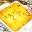 A hand scooping some Green Chile Cornbread Casserole out of the dish with a spoon