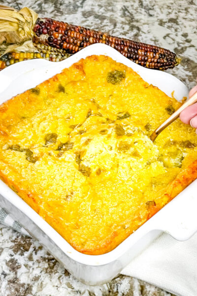 A hand scooping some Green Chile Cornbread Casserole out of the dish with a spoon