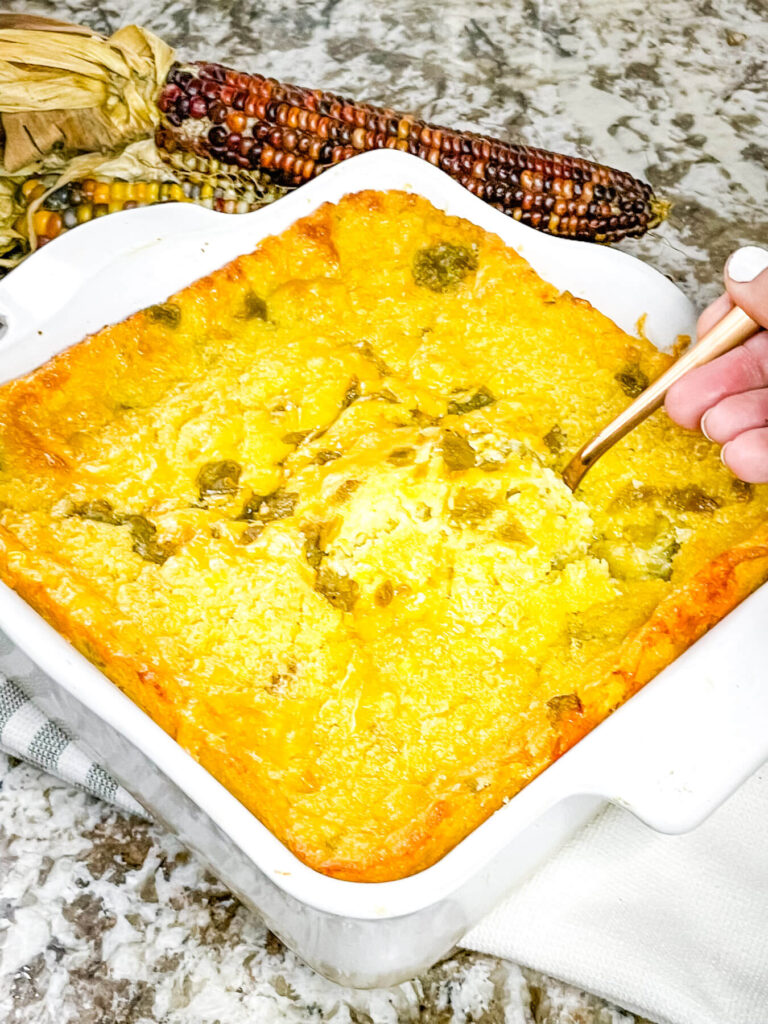 A hand scooping some Green Chile Cornbread Casserole out of the dish with a spoon