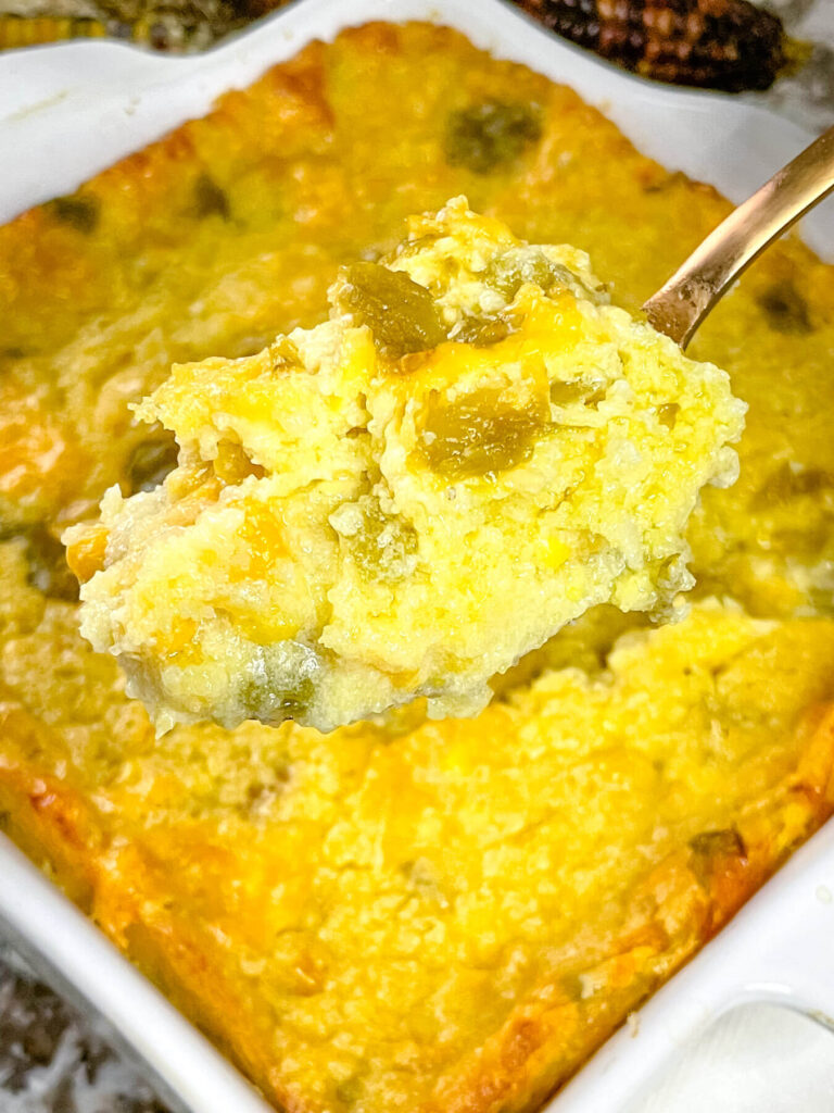 A spoon full of Green Chile Cornbread Casserole above the baking dish