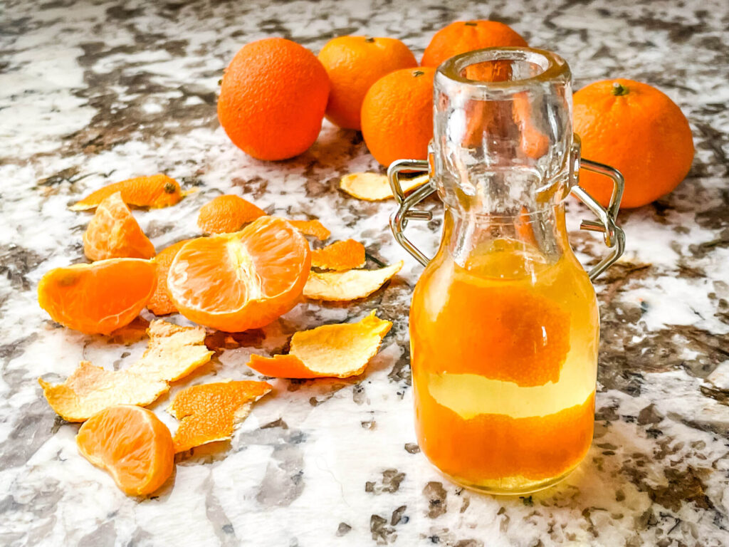 A bottle full of Orange Simple Syrup with peels and oranges around it
