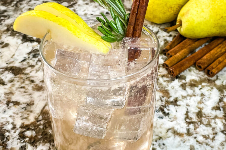 A clear glass with the Pear Tree Vodka Cocktail and garnished with pear, rosemary, and cinnamon stick